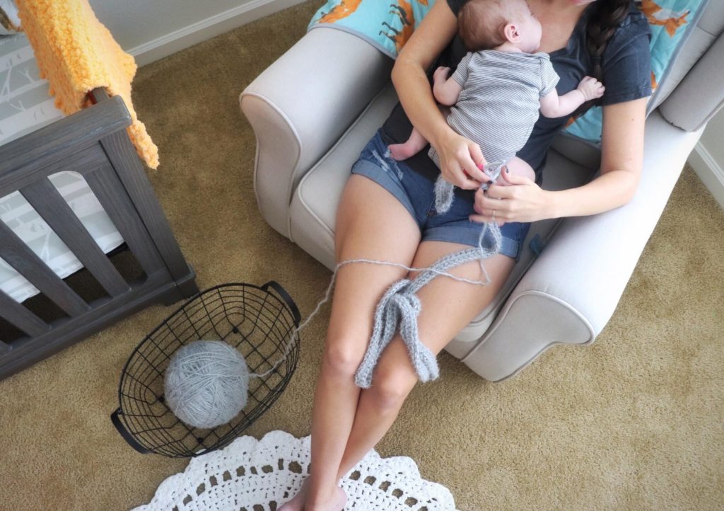 Sigoni crocheting the Cozy Hygge Blanket Wrap in the nursery with her baby boy laying on her chest