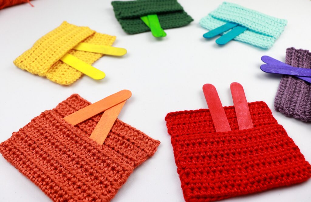 Six Crochet Color Pockets (a quick easy crochet toy for babies) in the colors red, orange, yellow, green, blue, and purple. Each pocket has two colorful popsicle sticks to match.