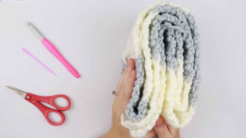 Screenshot from the Cheaters Gingham Blanket CAL Part 1 video tutorial showing Sigoni holding on the finished first panel of the crochet along. Also pictured is an 8mm crochet hook, tapestry needle, and scissors.