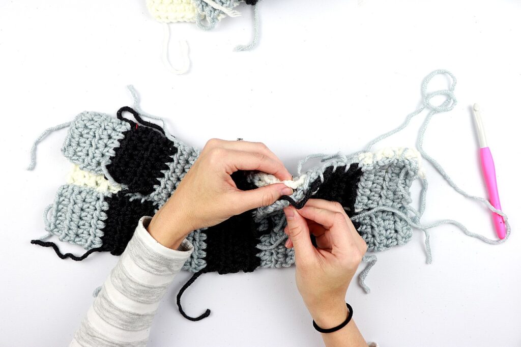 a photo of Sigoni's hands, showing how to sew together the half double crochet panels of the simple gingham style crochet pillow cover.