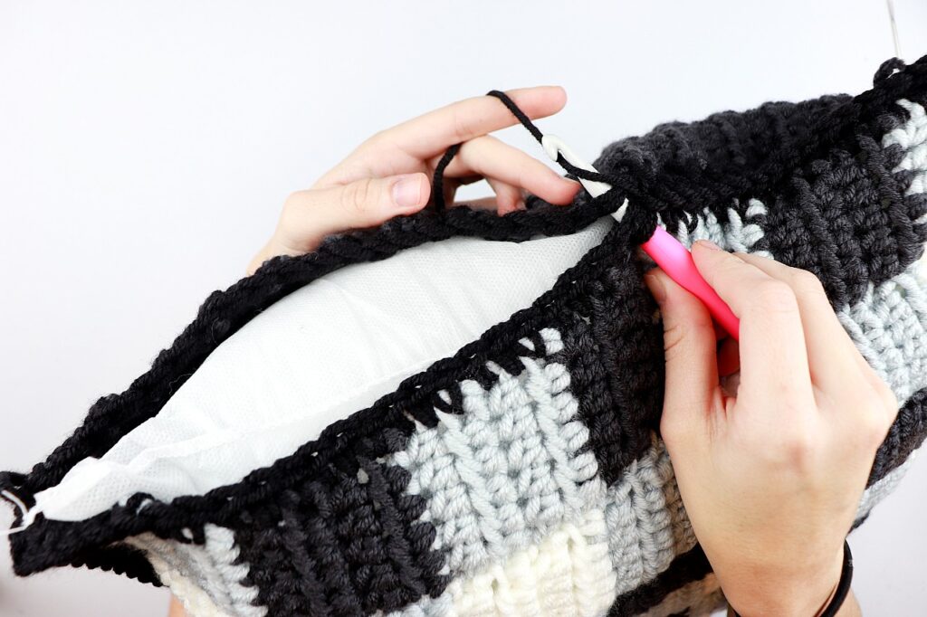 Sigoni showing how to sew together the last side of the crochet pillow cover with the 18x18 inch pillow form already stuffed inside.