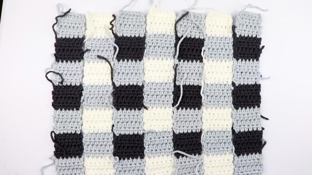 seven half double crochet panels using three different colors (grey, white, and black) of the simple gingham style crochet pillow cover.