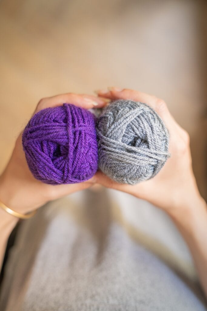 Girl holding two skeins of medium weight yarn in purple and gray