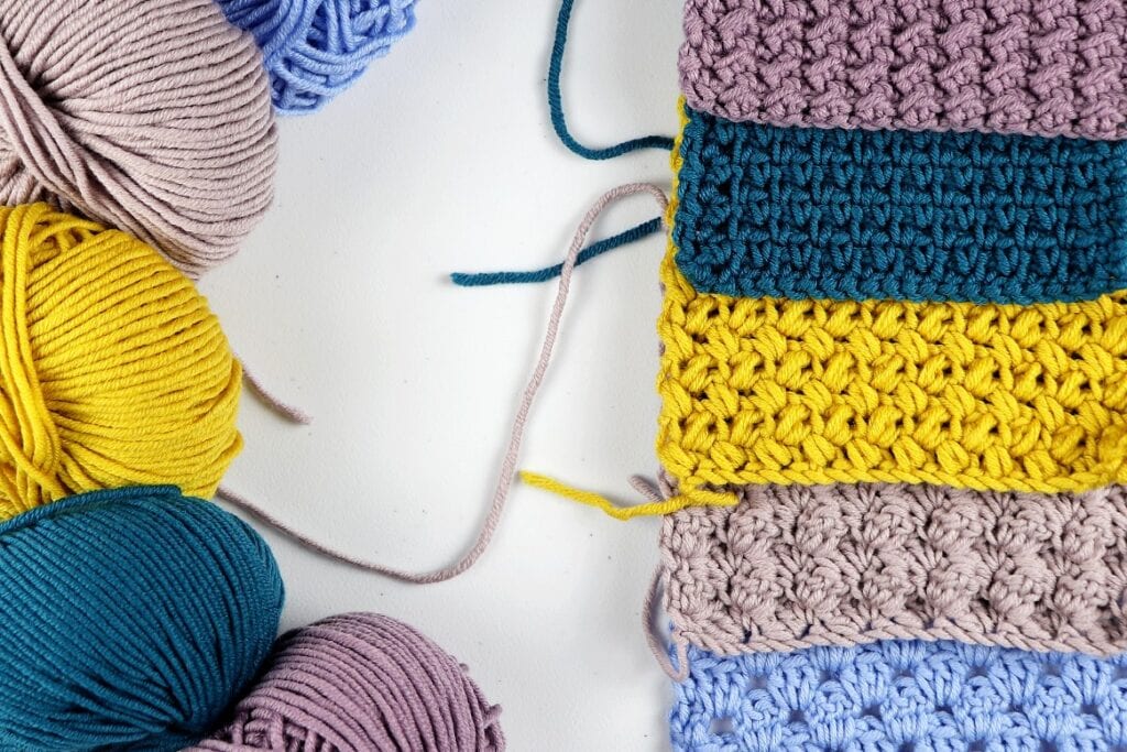 Showing the 5 beginner friendly crochet blanket stitches and the yarn used to make them. The swatches are purple, dark blue, yellow, tan, and light blue