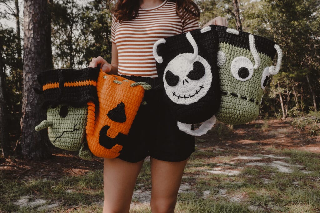 Sigoni holding four crocheted Halloween trick or treat bags. Witch, pumpkin, Jack skellington, and Frankenstein